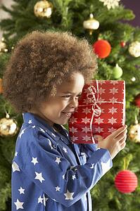 Young Boy Holding Gift In Front Of Christmas Tree
