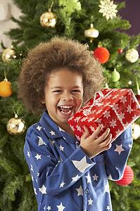 Young Boy Holding Gift In Front Of Christmas Tree