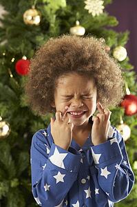 Young Boy Crossing Fingers In Front Of Christmas Tree