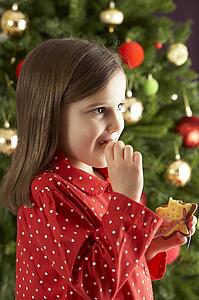 Young Girl Eating Star Shaped Christmas Cookie In Front Of Christmas Tree
