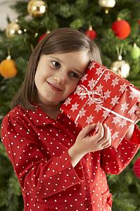 Young Girl Holding Gift In Front Of Christmas Tree