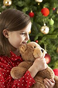 Young Girl Cuddling Teddy Bear In Front Of Christmas Tree