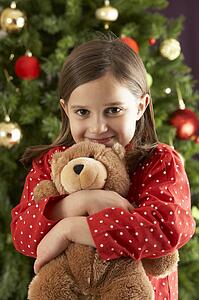 Young Girl Cuddling Teddy Bear In Front Of Christmas Tree
