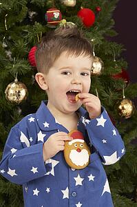 Young Boy Eating Cookie In Front Of Christmas Tree