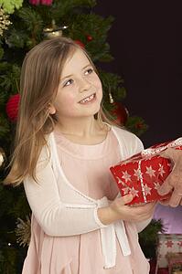 Young Girl Holding Christmas Present In Front Of Christmas Tree