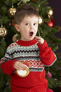 Young Boy Eating Cookie In Front Of Christmas Tree