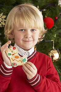 Young Boy Eating Cookie In Front Of Christmas Tree