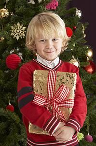 Young Boy Holding Gift In Front Of Christmas Tree
