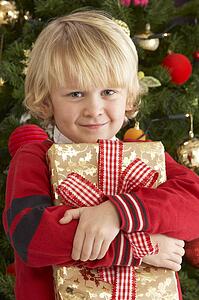 Young Boy Holding Gift In Front Of Christmas Tree