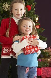 Two Young Girls With Presents In Front Of Christmas Tree