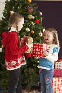 Two Young Girls With Presents In Front Of Christmas Tree