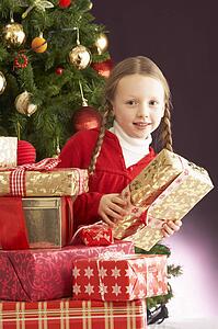 Young Girl Holding Christmas Present In Front Of Christmas Tree