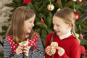 Two Young Girls Eating Cookies In Front Of Christmas Tree
