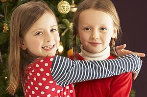 Two Young Girls Hugging In Front Of Christmas Tree