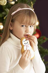 Young Girl Eating Cookie In Front Of Christmas Tree
