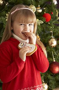 Young Girl Eating Cookie In Front Of Christmas Tree