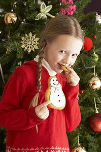 Young Girl Eating Cookie In Front Of Christmas Tree