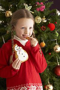 Young Girl Eating Cookie In Front Of Christmas Tree