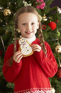 Young Girl Eating Cookie In Front Of Christmas Tree