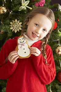 Young Girl Eating Cookie In Front Of Christmas Tree