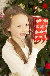 Young Girl Holding Christmas Present In Front Of Christmas Tree