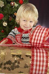 Young Boy Holding Gift In Front Of Christmas Tree