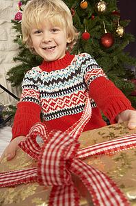 Young Boy Holding Gift In Front Of Christmas Tree