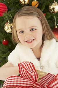 Young Girl Holding Gift In Front Of Christmas Tree