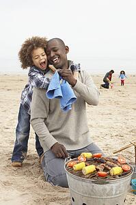 Young Family Enjoying Barbeque On Beach