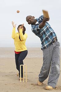 Young Couple Playing Cricket On Autumn Beach Holiday