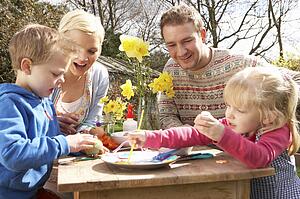 Family Decorating Easter Eggs On Table Outdoors 