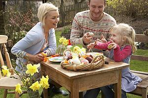 Family Decorating Easter Eggs On Table Outdoors 