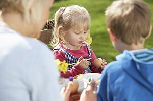 Mother And Children Decorating Easter Eggs On Table Outdoors 