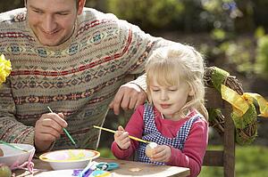 Father And Daughter Decorating Easter Eggs On Table Outdoors 