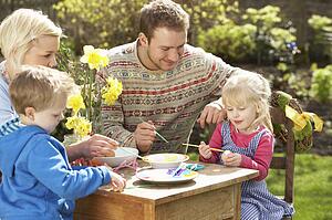 Family Decorating Easter Eggs On Table Outdoors 