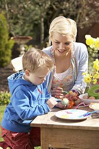Mother And Son Decorating Easter Eggs On Table Outdoors 