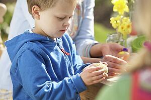 Mother And Children Decorating Easter Eggs On Table Outdoors 
