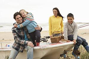 Family Group Sitting On Boat With Fishing Rod On Winter Beach