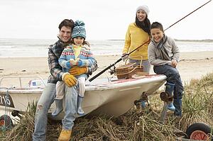 Family Group Sitting On Boat With Fishing Rod On Winter Beach