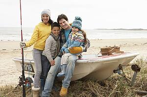 Family Group Sitting On Boat With Fishing Rod On Winter Beach