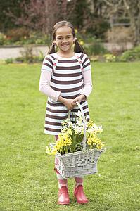 Girl Holding Basket Of Daffodils In Garden