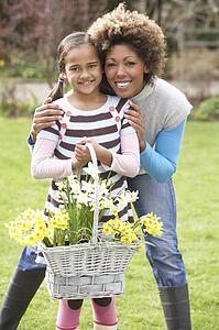 Mother And Daughter Holding Basket Of Daffodils In Garden