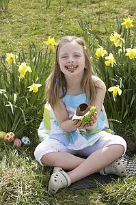 Girl Eating Chocolate Egg On Easter Egg Hunt In Daffodil Field