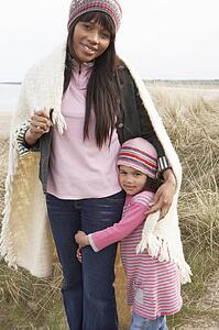 Mother And Daughter Wrapped In Blanket Amongst Dunes On Winter Beach