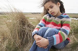 Young Girl Sitting Amongst Dunes On Winter Beach
