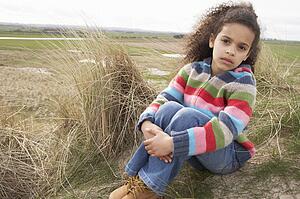Young Girl Sitting Amongst Dunes On Winter Beach