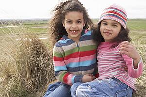 Young Girls Sitting Amongst Dunes On Winter Beach