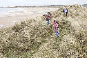 Family Walking Along Dunes On Winter Beach