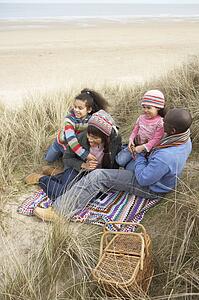 Family Sitting In Dunes Enjoying Picnic On Winter Beach