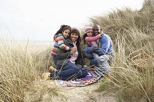Family Sitting In Dunes Enjoying Picnic On Winter Beach